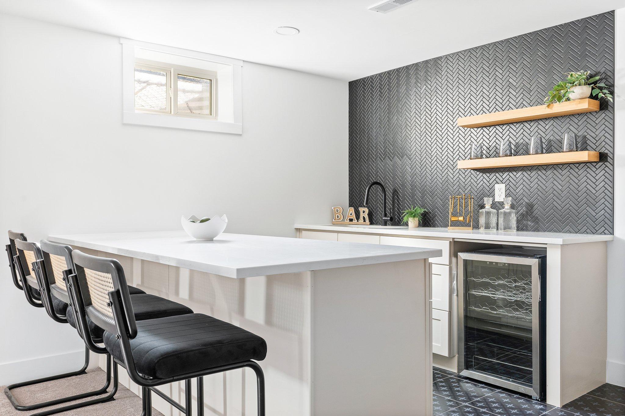 White basement bar with dark gray herringbone mosaic backsplash.